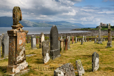 Ancient tombstones at Kilpatrick Cemetery next to Duart Castle on Isle of Mull with sailboats on Sound of Mull at Loch Linnhe Sc
