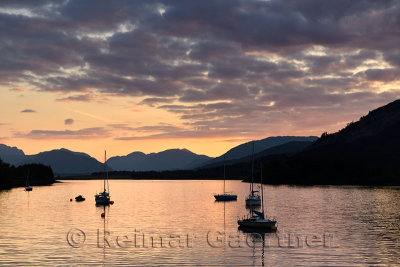 Moored sailboats on Loch Leven with red sky sunset clouds at Glencoe Boat Club and distant Sgurr Dhomhnuill peaks Scottish Highl