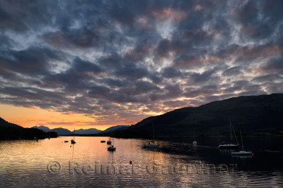 Red Sunset with clouds on Loch Leven with moored sailboats at Glencoe Boat Club and distant mountains of Scottish Highlands Scot