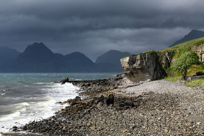 Rocky shore at Port na Cullaidh harbour Elgol with Red Cuillin Mountains under clouds at Loch Scavaig Isle of Skye Scotland UK