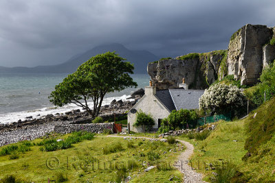 House under cliff at Elgol beach with Red Cuillin Mountains under clouds at Loch Scavaig Scottish Highlands Isle of Skye Scotlan