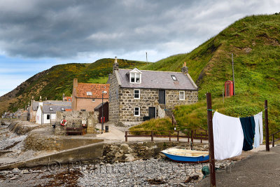 Single row of houses of Crovie coastal fishing village on Gamrie Bay North Sea Aberdeenshire Scotland UK with red telephone box 