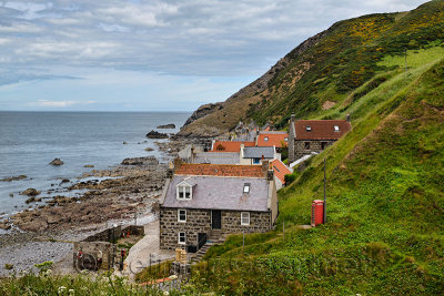 Single row of houses of Crovie coastal fishing village on Gamrie Bay North Sea Aberdeenshire Scotland UK with red telephone box