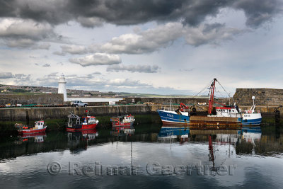 Fishing boats and lighthouse at MacDuff Harbour Shipyards with view of Banff over Banff Bay Aberdeenshire Scotland UK