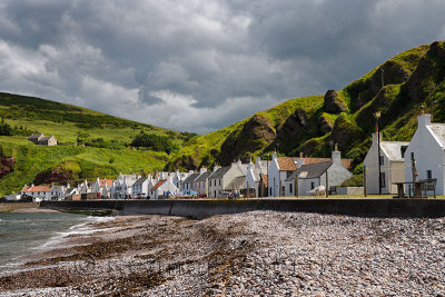 Stone beach and row of white houses of Pennan coastal fishing village on North Sea in Aberdeenshire Scotland UK with green sea c