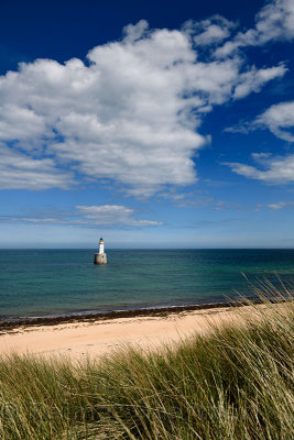 Rattray Head Lighthouse in the North Sea at Buchan Aberdeenshire Scotland with blue sky and white cloud from sea grass sand dune