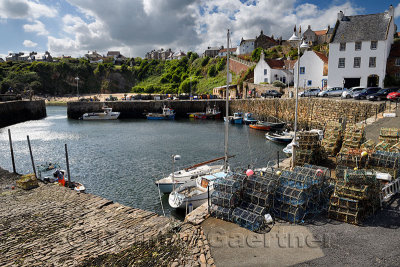 Stone pier walls at Crail Harbour with fishing boats and lobster traps and cliff with beach at Crail Fife Scotland UK
