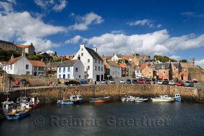 Boats moored at stone pier in Crail Harbour with Crail House lookout turret over the North Sea in Fife Scotland UK