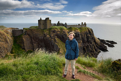 Scottish female tourist visitor at top of cliff above Old Hall Bay with Donnottar Castle ruins on the North Sea Scotland UK