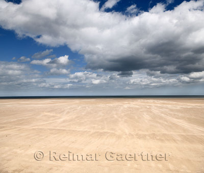 Blowing sand in High wind on wide St Andrews West Sands beach with blue sky and white clouds and North Sea at St Andrews Fife Sc