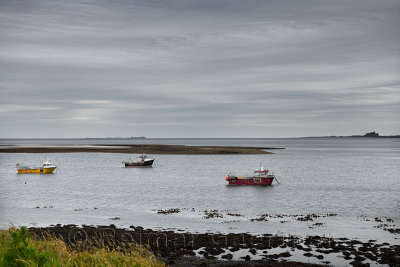 Three boats at low tide on Holy Island of Lindisfarne with Bamburgh Castle and Farne Islands on the North Sea England UK