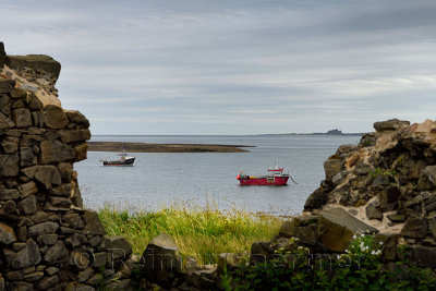 Two fishing boats at low tide in the Harbour of Holy Island of Lindisfarne with Bamburgh Castle through the Steel End ruins Engl