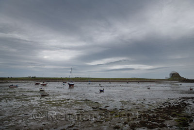 The Ouse with anchored boats at low tide from Willy Pots Rock on Holy Island with Lindesfarne Castle under renovation England UK