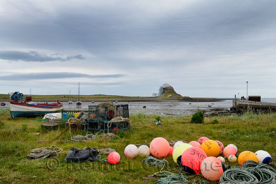 Bright fishing bouys and lobster pots on shore at The Ouse bay on Holy Island with Lindisfarne Castle under renovation England U