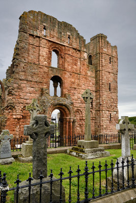 Red stone front of Lindisfarne church ruins of the medieval priory with cemetery tombstones on Holy Island of Lindisfarne Englan