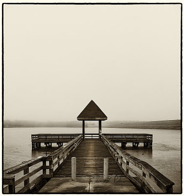 The Lake Zorinsky pier on a cold foggy winters day. The lake is frozen over but the ice isn't thick enough yet to support fishing. It always seems to me as if nature goes quiet on the foggy days.

An image may be purchased at http://edward-peterson.pixels.com/featured/lake-zorinsky-pier-edward-peterson.html?newartwork=true