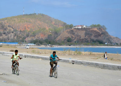 Cyclists along Tasi Tolu beach with Dili Rock in the background