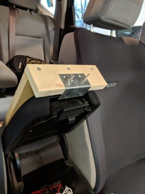 Since the front bracket is positioned on the armrest that is attached to the top of the lid to the console, it is out of the way of the lever that opens the console lid.