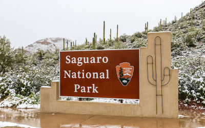 Park entrance sign with the snow blanketed Red Hills in the background in Saguaro National Park