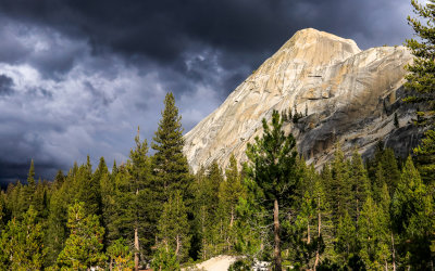 Sun illuminates a granite peak along the Tioga Road as dark snow clouds form in Yosemite National Park
