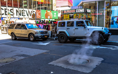 Steam seeps from the street through a manhole cover in Times Square