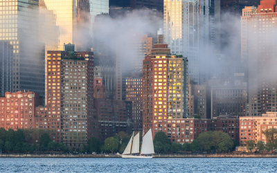 Sailboat glides past a foggy NYC Skyline as the last rays of sun reflect off of building windows
