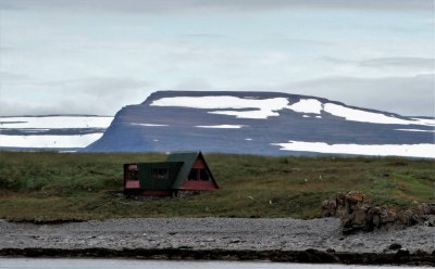Random house beneath mountain seen while traveling to Vigur Island