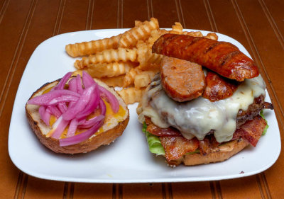 A Bacon, Hot Italian sausage, Cheese Burger With lettuce, tomato, pickled onions on a homemade Pretzel Bun w/fries
