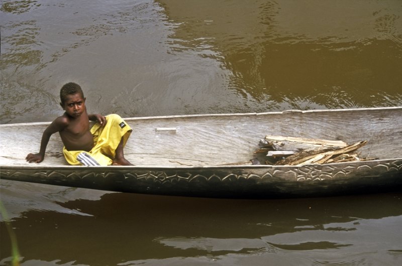 Kamoro boy afloat in a dugout canoe
