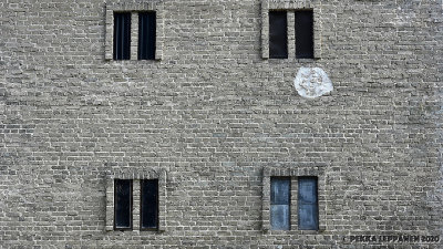 Six (?) windows and a filled hole in a brick wall