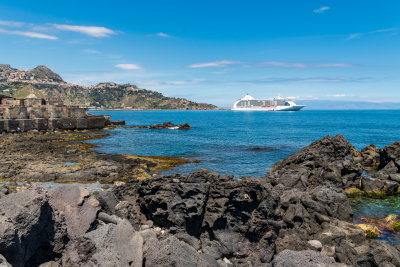 Lava rock on the coast, Naxos, Sicily.  The Regent Seven Seas Voyager anchored in the bay.
