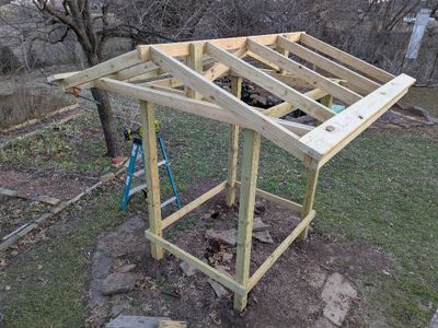 Then I cut a couple of 8'x2x6 boards to exactly 96 and put together 2 stop blocks made by screwing a piece of 1x4 onto a 2x4 block. The latter I clamped onto each end of my 'plate' to act as spacers to hold each 2x6 board in place with about a 1 lap over the bottom edge of the roof to provide a drip line. I measured down from the top of the ridge board, adjusted the 2x6 alignment a bit, to ensure it was parallel to the ridge line, and screwed each into place.