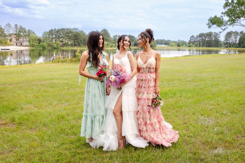 Bride with Bridesmaids on open grassy area in front of a lake