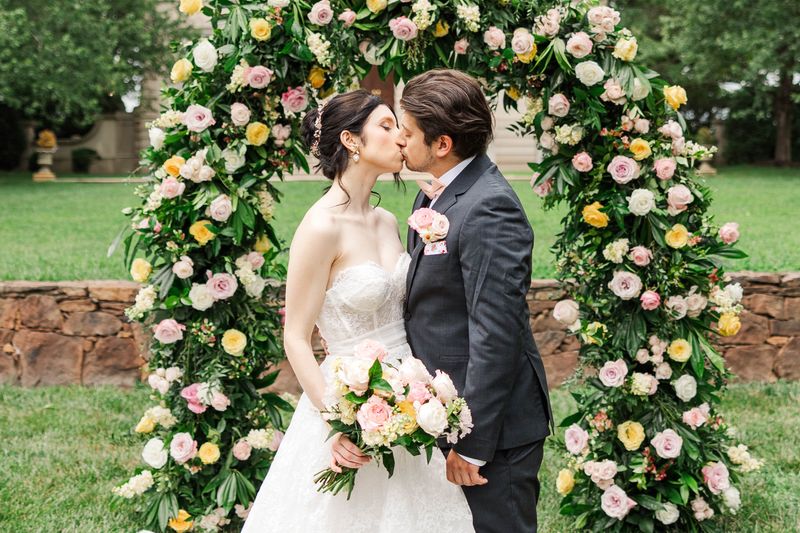 Bride and Groom kissing in front of floral arch in summer time