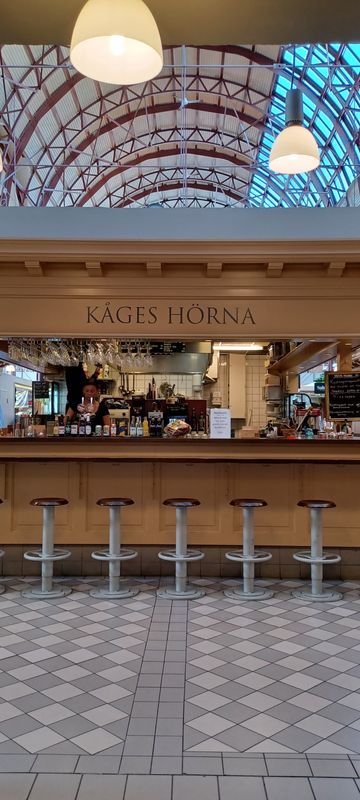 Old-fashioned gourmet food hall with vendors offering cheeses, baked goods, deli sandwiches & more