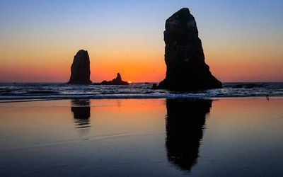 The Needles are reflected in the sand and surf as the sun sets on Cannon Beach