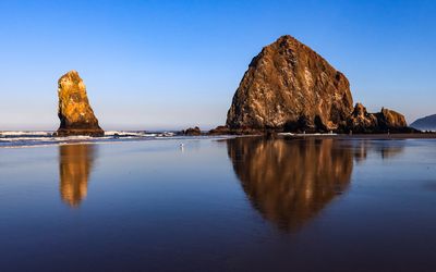 A Needle and Haystack Rock reflected in the sand and surf at sunrise on Cannon Beach