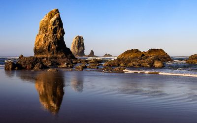 The Needles and other sea stacks reflected in the sand and surf at sunrise on Cannon Beach