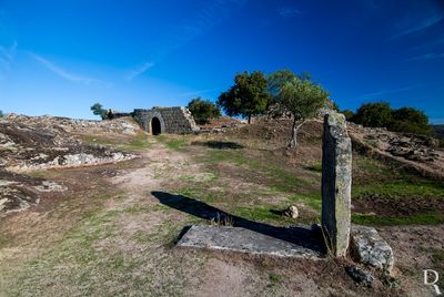 Na pedra de cabeceira descobrimos uma inscrição, quase ilegível, que conta a história do oficial que ali foi sepultado. “Aqui jaz Miguel Augusto de Sousa Mendonça Corte Real, fidalgo da Casa Real e Comendador das Ordens de: São Bento de Avis e de Nossa Senhora da Conceição, condecorado com a medalha da Torre Espada, de Valor, Lealdade e Mérito, e com a Cruz de S. Fernando, dada por sua Majestade Católica, Tenente Coronel, Comandante de Infantaria n.º 6, filho do Tenente General e Conselheiro de Guerra, João de Sousa Mendonça Corte-Real. Nasceu em 23 de agosto de 1803, foi barbaramente assassinado pelos seus próprios soldados em 12 de setembro de 1840”.
Consta que a causa deste homicídio foi o eventual incumprimento de uma promessa que fizera aos seus soldados.
https://www.aldeiashistoricasdeportugalblog.pt/2019/04/13/a-misteriosa-pedra-tumular-do-oficial-sepultado-na-aldeia-historica-de-castelo-mendo/