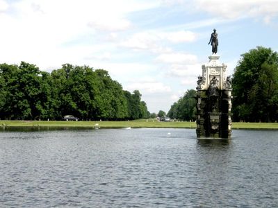 Looking across the pond is a long straight road down to a gate.