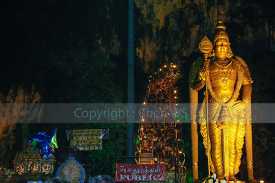 Lord Muruga watches over. Kavadi carriers can be seen climbing up the steps to the cave temple