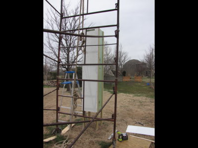 I leveled and screwed a board, horizontally, 8' from the top of the tower (it's lying on the ground next to the piece about to go up, in this photo), then set the siding on the cross piece while I screwed the siding into place.