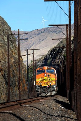 A BNSF train rolls through a cut guarded with rock fall warning fences.