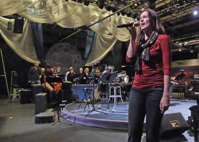 ERIN SINGS AT THE TECH REHEARSAL, WITH THE CHORUS IN THE BACKGROUND