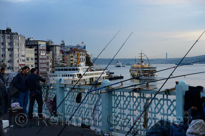 Turkish men fishing on Galata Bridge with Karakoy Pier and early morning sea bus on Boshphorus Istanbul
