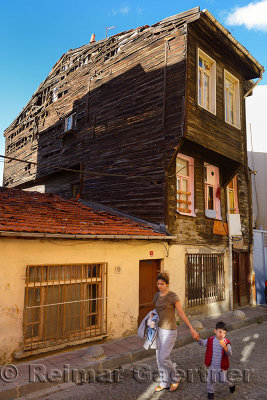 Woman and child walking by old run down Historic Ottoman wooden house in Istanbul Turkey