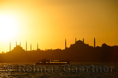 Blue Mosque and Hagia Sophia minarets silhouettes at sundown over the Bosphorus with backlit boat Istanbul