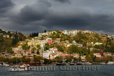 Sun on homes on a hillside of Arnavutkoy Besiktas Istanbul with storm clouds on the Bosphorus Strait