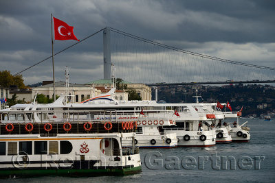 Ferry and tour boats at Besiktas Pier with the First Bosphorus Bridge and Turkish flag