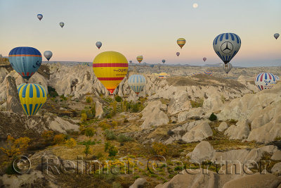 Many hot air balloons over the Red Valley with cave churches Cappadocia Turkey at dawn with moon